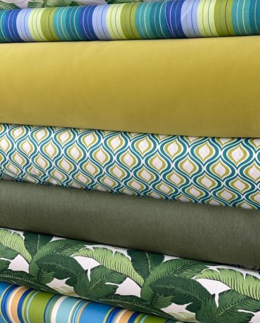 Four fabric rolls with solid, geometric, and floral patterns in green and blue hues.