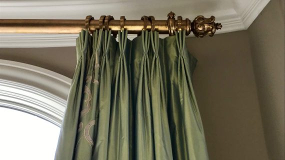 Elegant green curtains hanging from a decorative brass curtain rod.